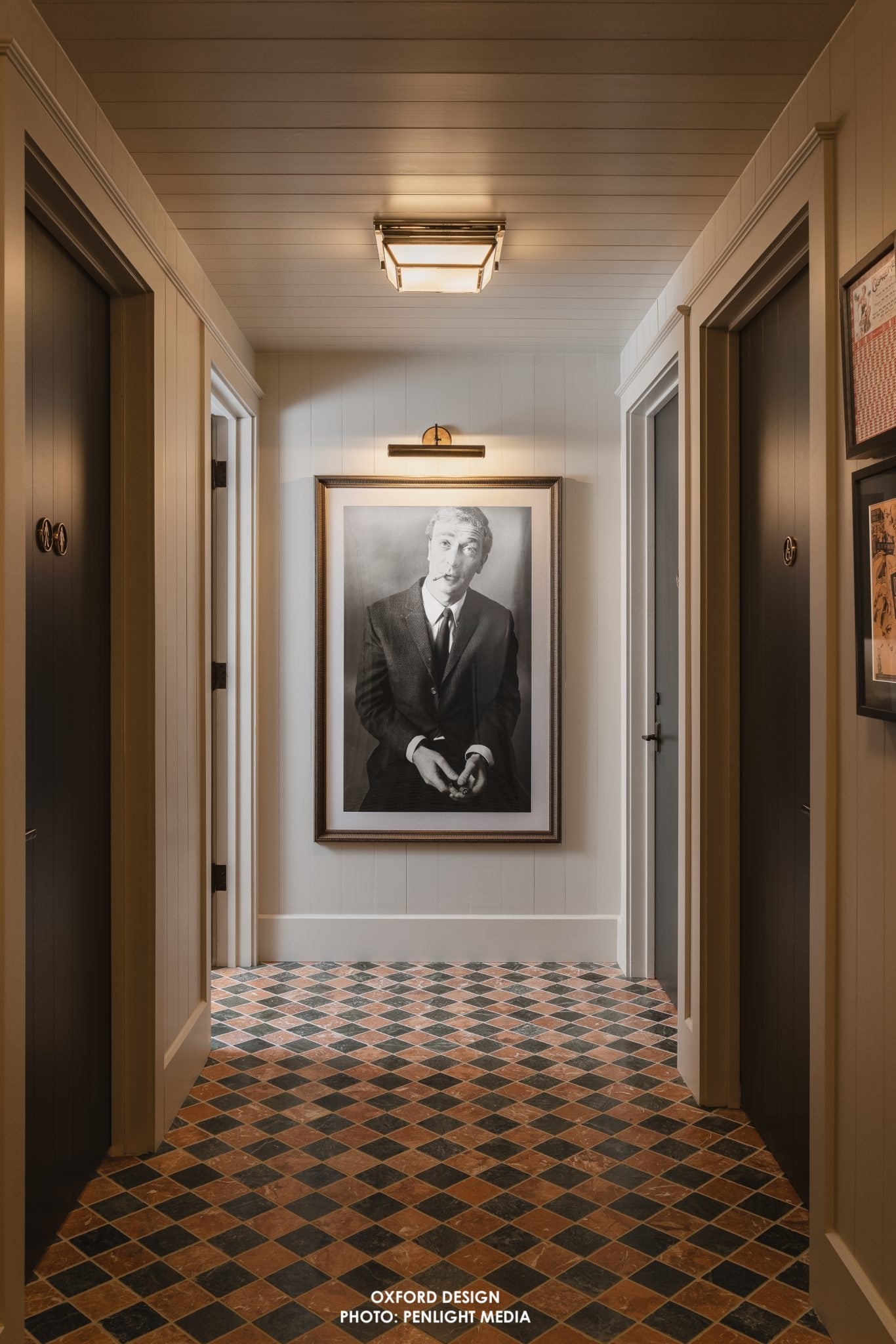 Hallway with a framed portrait on the wall, checkered floor, and ceiling light fixture.